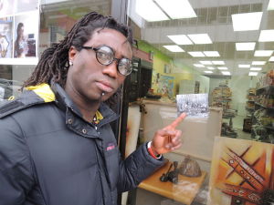Marcellin Gbazaï, propriétaire de l'épicerie Mon Afrique au Saguenay, pointe un autocollant de la Fédération des Québécois de souche dans la vitrine de son commerce | Photo : via le Journal de Québec
